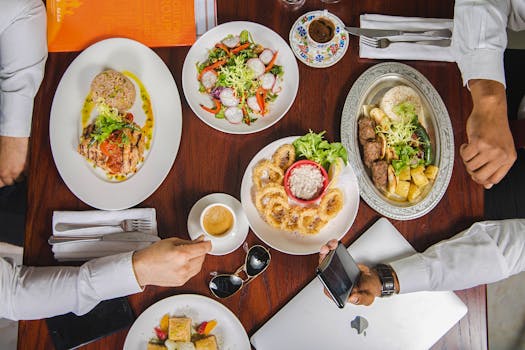 Overhead shot of diverse gourmet meals on a wooden table in a Dubai restaurant with people dining.