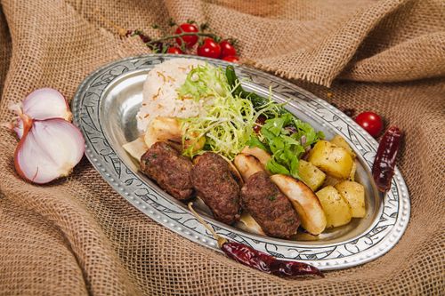 Free An appetizing Mediterranean dish featuring grilled meat, rice, potatoes, and fresh salad on a decorative platter. Stock Photo
