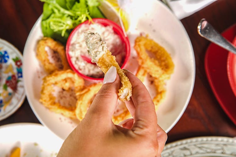 Person Dipping A Cooked Food On Sauce