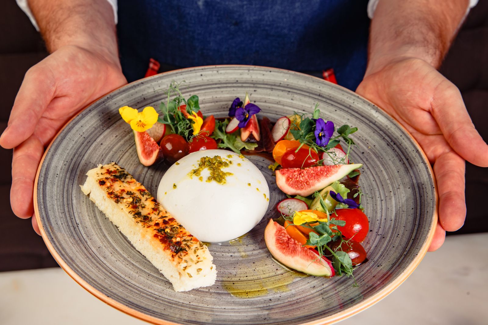 A plate of burrata, figs and heirloom tomatoes held by a private chef