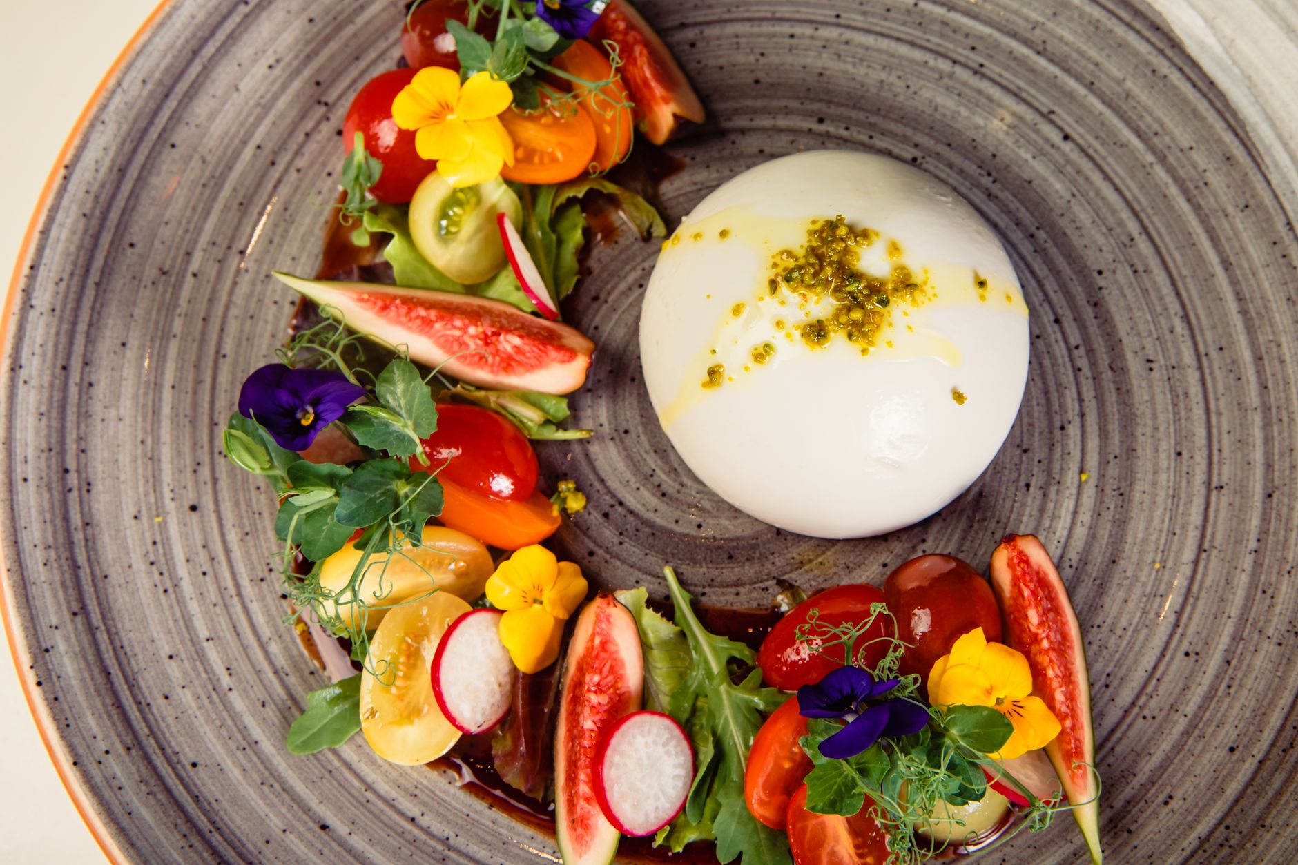 A vibrant dish featuring fresh vegetables and creamy burrata cheese on a decorative plate.