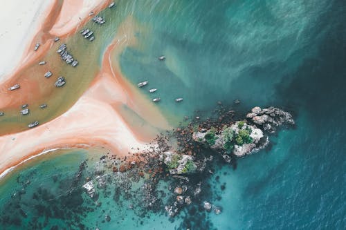 Spectacular drone view of boats floating on surface of turquoise ocean water washing sandy beach on sunny day