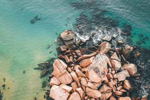 Free Picturesque drone view of transparent water of turquoise sea with waves crashing near rough stony boulders on sunny day Stock Photo