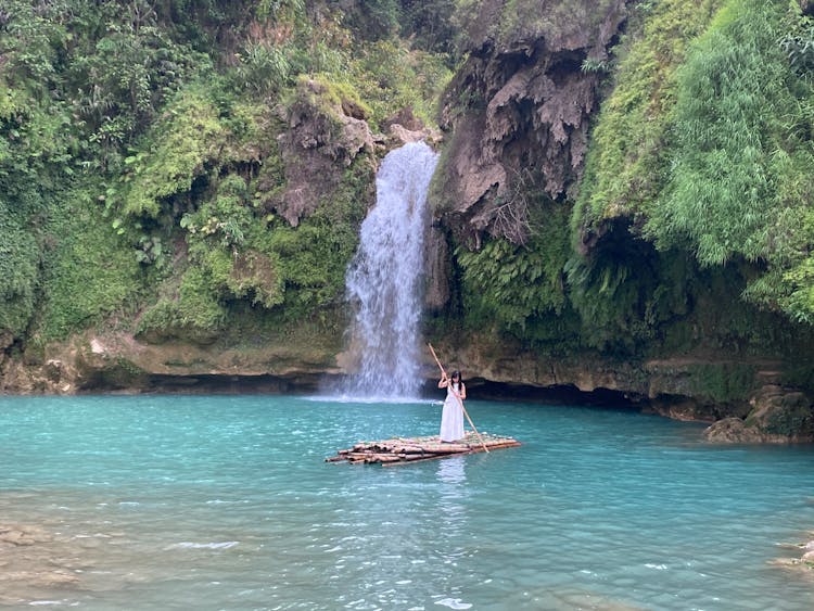 Woman Floating On Raft With Oar Against Waterfall