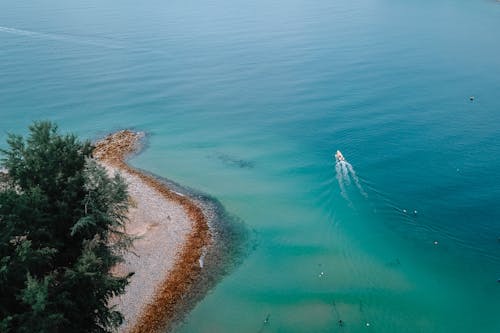 Picturesque aerial view of yacht sailing on amazing turquoise sea near coastline with green trees in sunlight