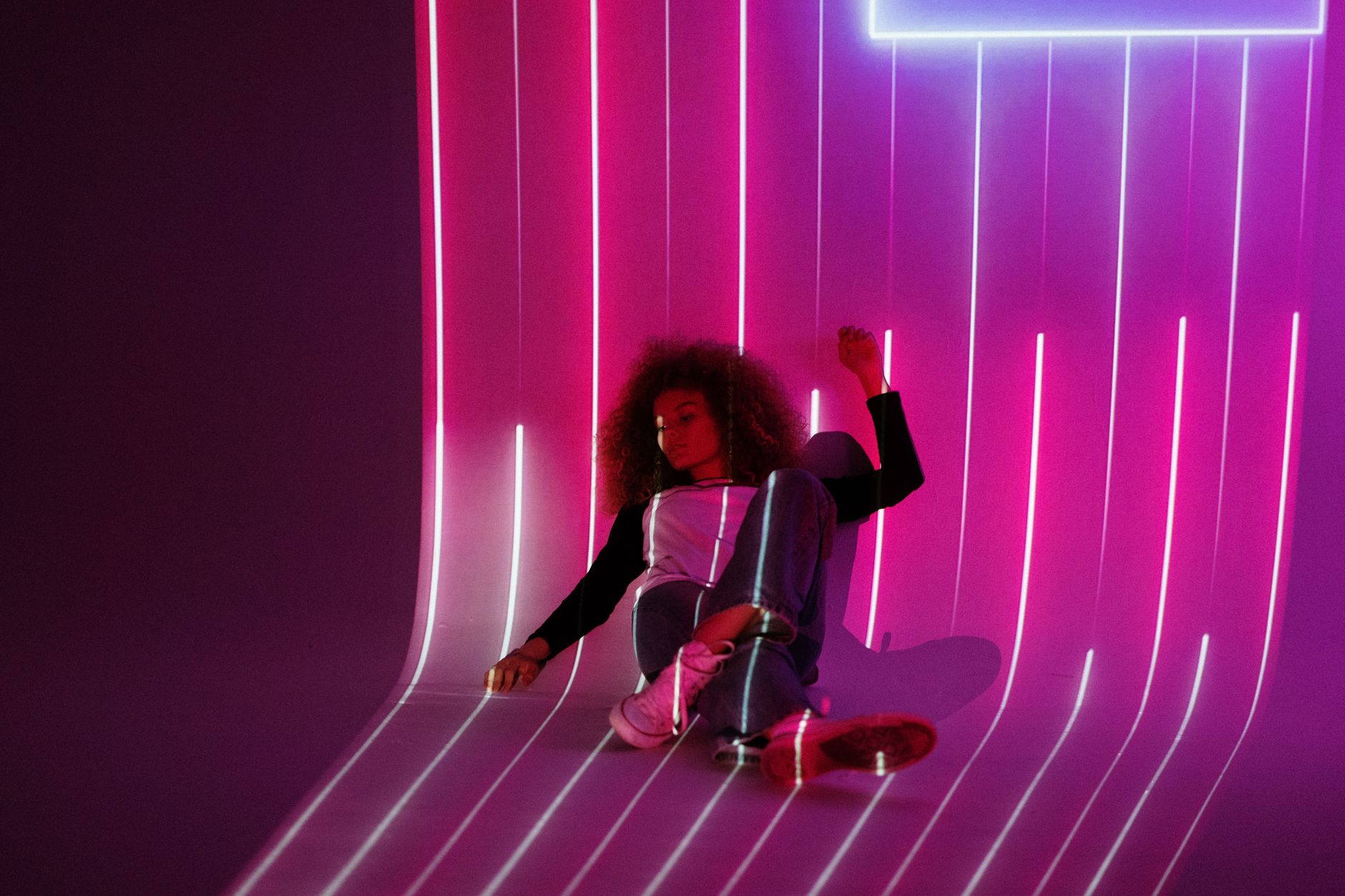 A woman sits amid a vibrant neon light projection creating futuristic art indoors.