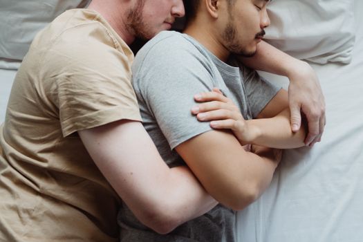 一对跨种族同性恋夫妇闭着眼睛，依偎在床上，享受着放松的温柔时刻