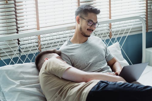 Free Man Cuddling Another Man Using a Laptop in Bed Stock Photo