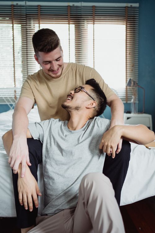 Free Interracial gay couple smiling and sharing a loving moment while sitting together indoors. Stock Photo