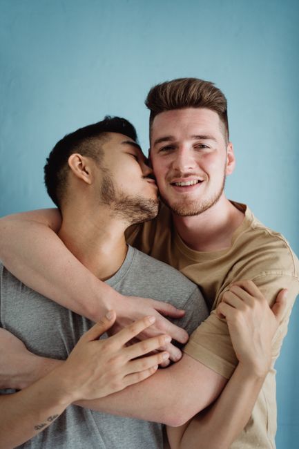 Interracial gay couple embracing with affection and love against a blue background.