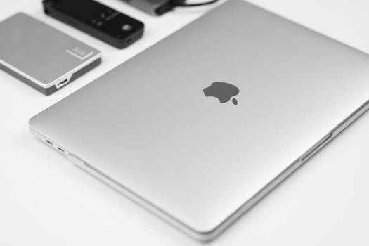 Minimalist flat lay of a silver laptop with tech accessories on a white surface.