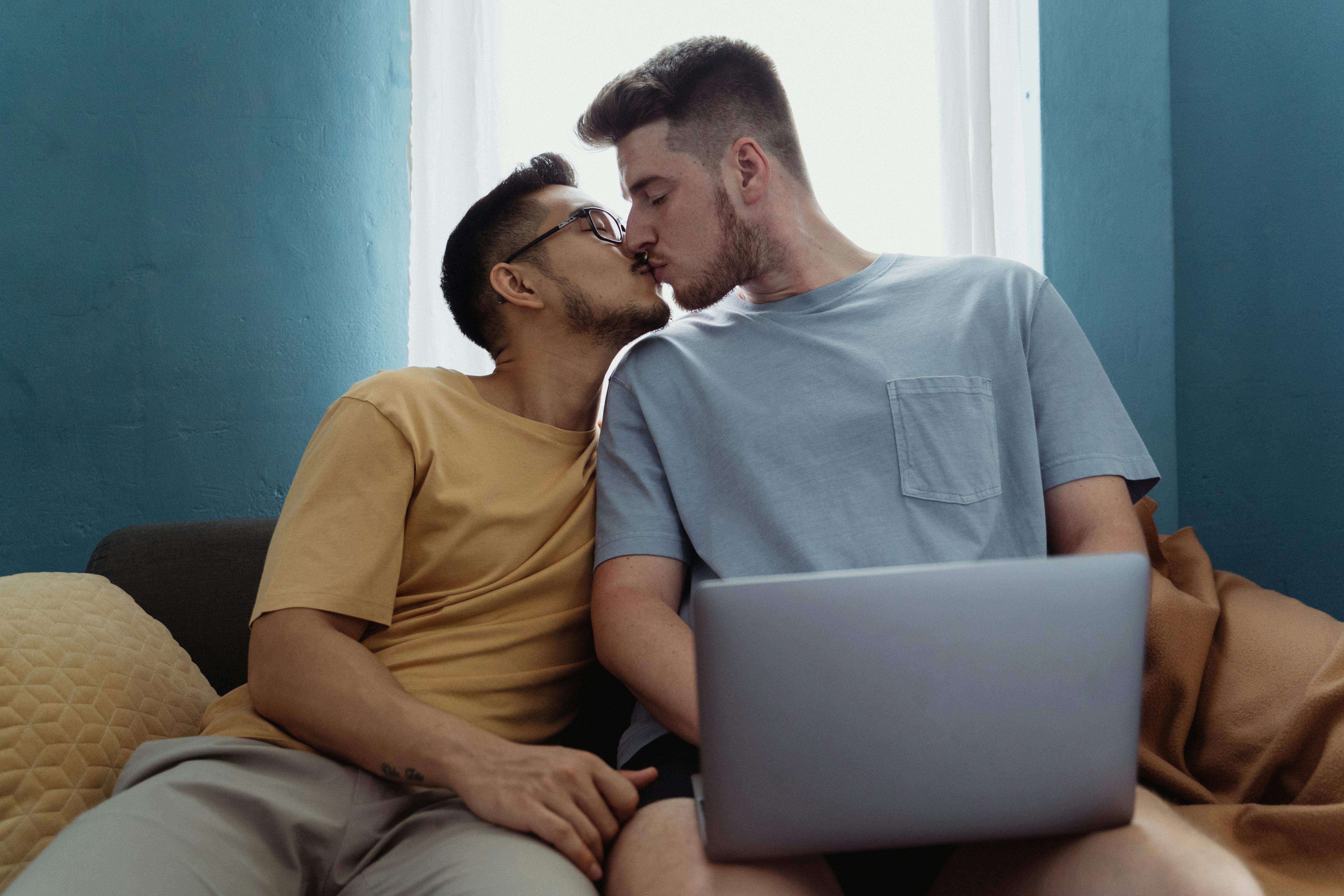 two men sitting on a sofa and kissing