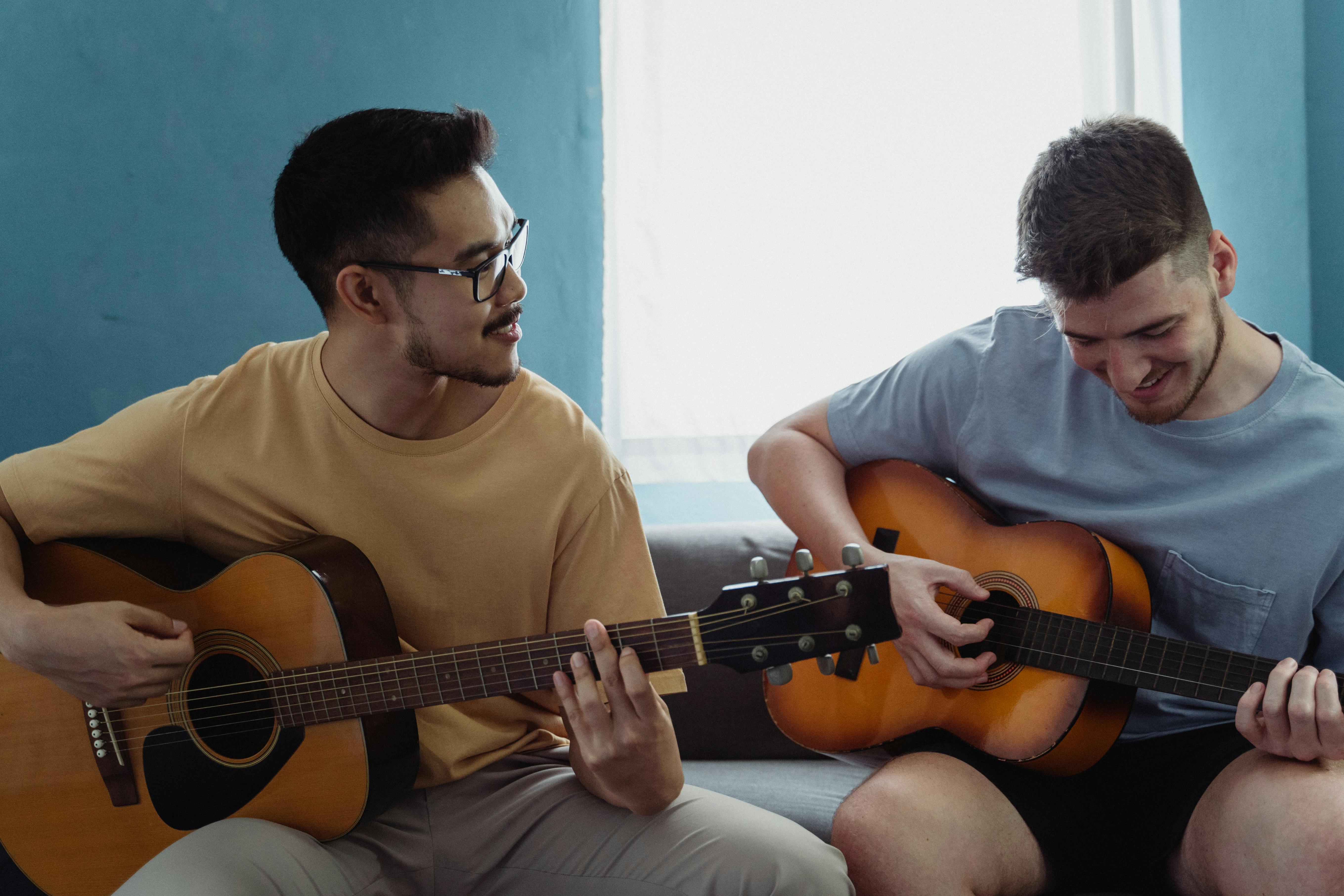 两个年轻人在室内弹着原声吉他，共享音乐时光