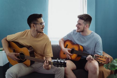 Free Two men enjoying playing acoustic guitars together on a sofa in a cozy indoor setting. Stock Photo