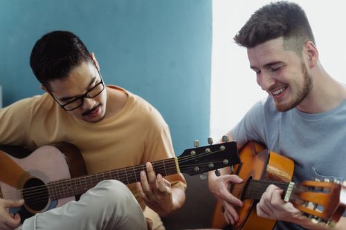 Free Two smiling men enjoying music while playing acoustic guitars together indoors. Stock Photo