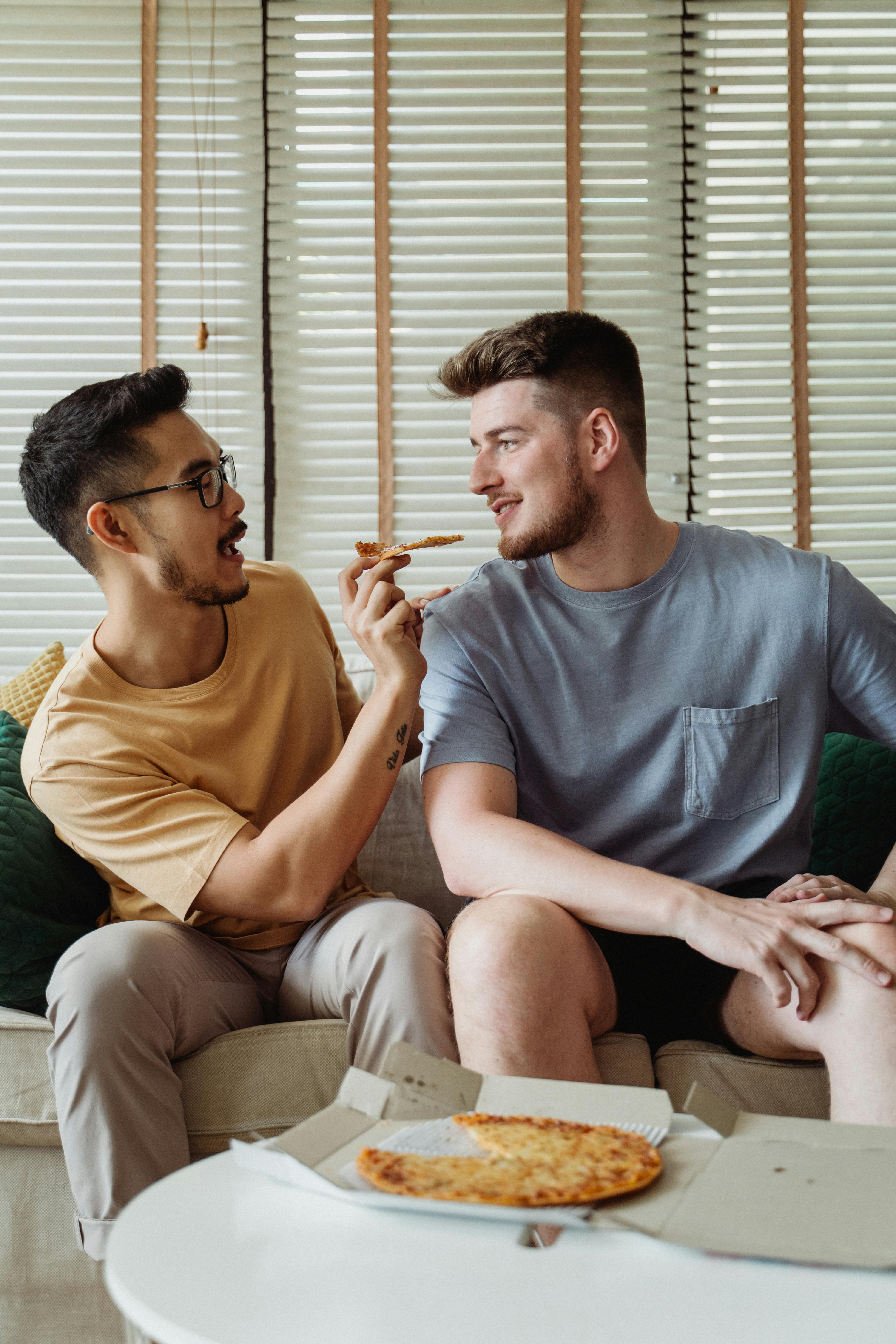 man feeding pizza to another man