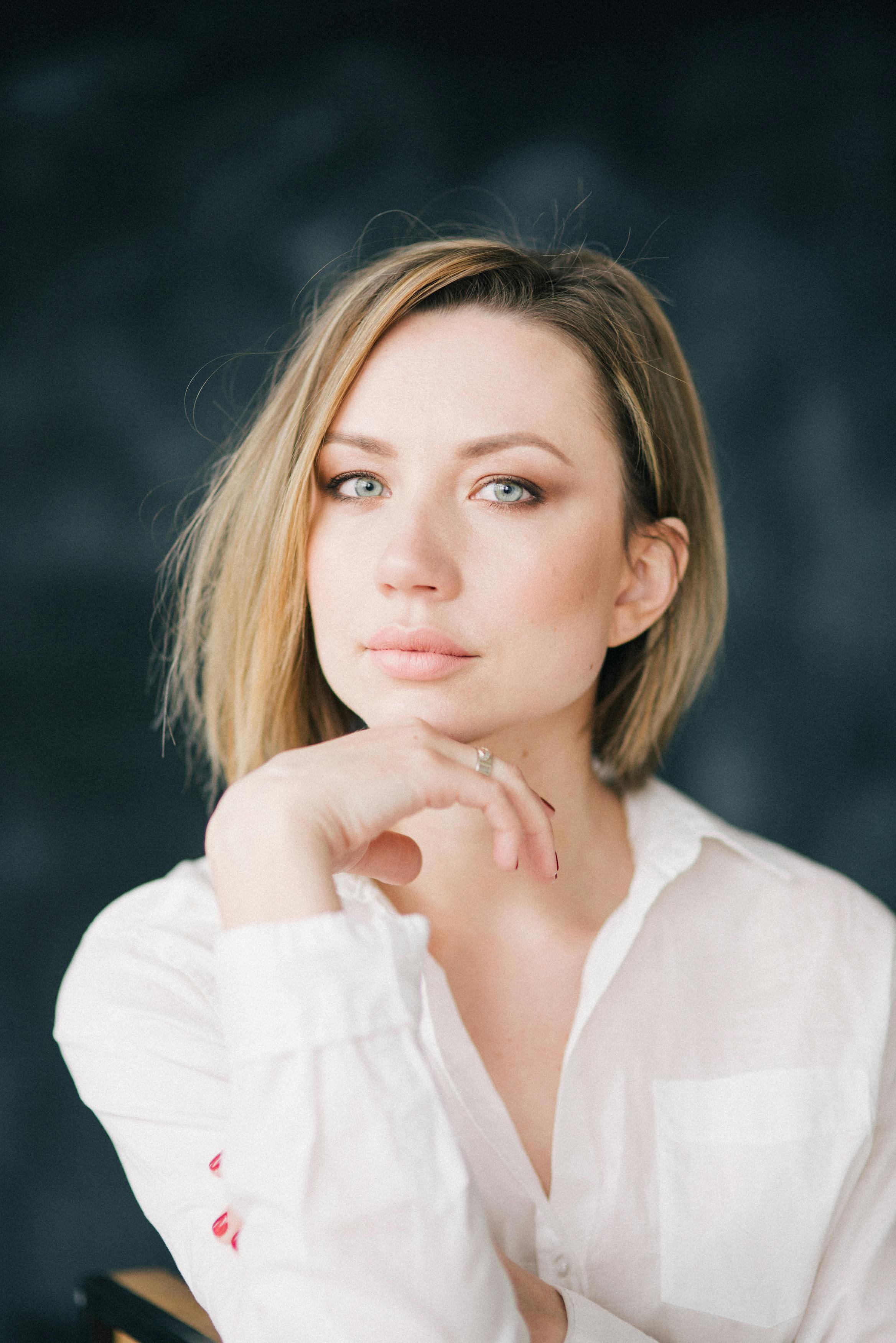 一位留着金色短发的白人女子摆出时尚肖像的姿势，手放在下巴上