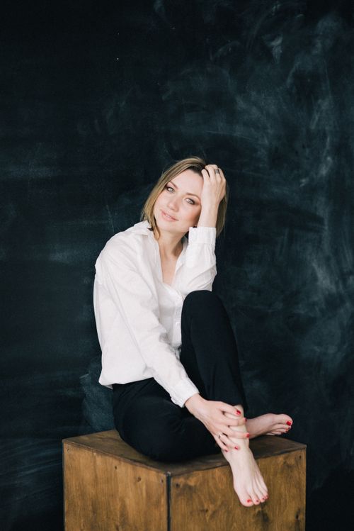 Free A stylish woman in a white shirt and black pants sitting on a wooden box against a dark background. Stock Photo