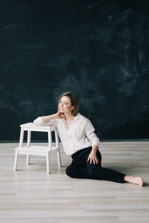 Free A woman in white blouse and black pants poses thoughtfully in a minimalist studio with a blackboard wall. Stock Photo