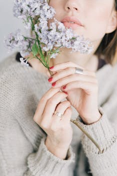 这是一幅特写肖像，画中的女人留着红指甲，手拿精致的丁香花，身穿舒适的毛衣
