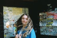 Cheerful female with flowing hair in denim jacket looking away while standing on street near walls with shabby bulletin boards