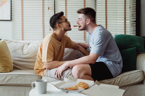 Two Men Sitting on a Couch and Eating Pizza