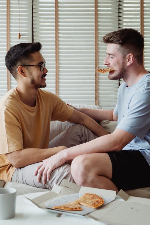 Man Looking at Another Man Eating Pizza