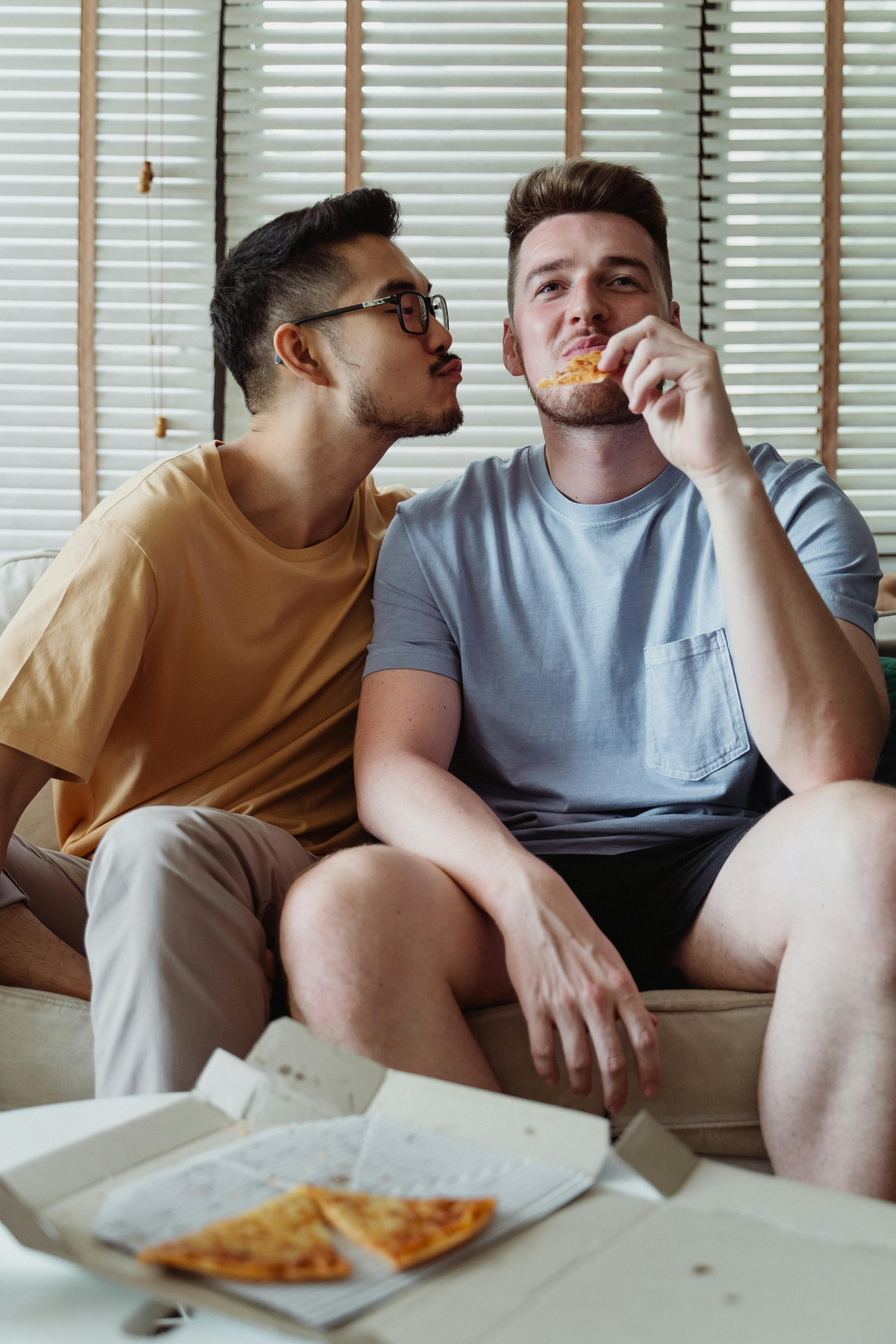 man trying to kiss a man eating pizza