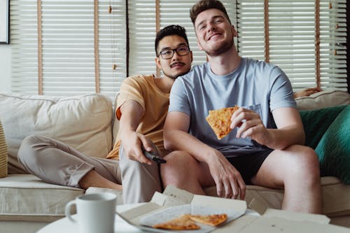 Two Men Relaxing on a Couch and Eating Pizza