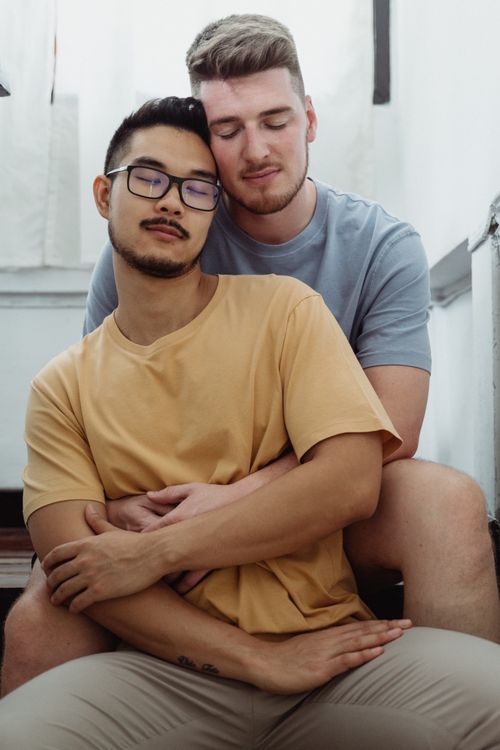 Free A romantic embrace between an interracial gay couple sitting indoors, conveying love and togetherness. Stock Photo