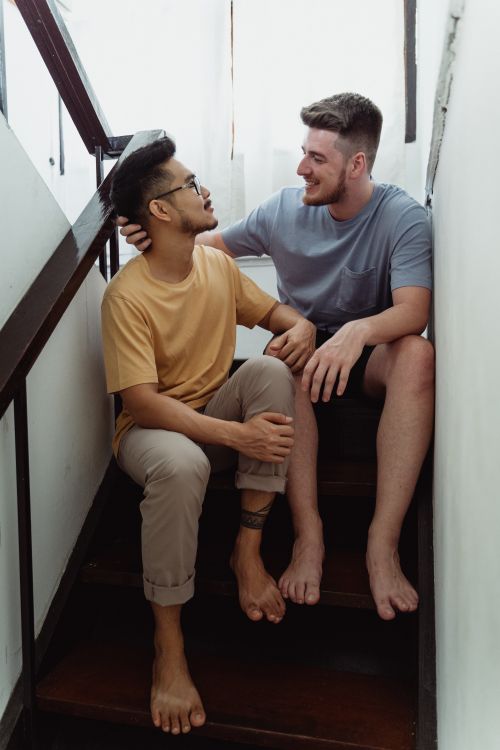 Free Interracial gay couple sitting on stairs, sharing a moment of happiness and togetherness. Stock Photo
