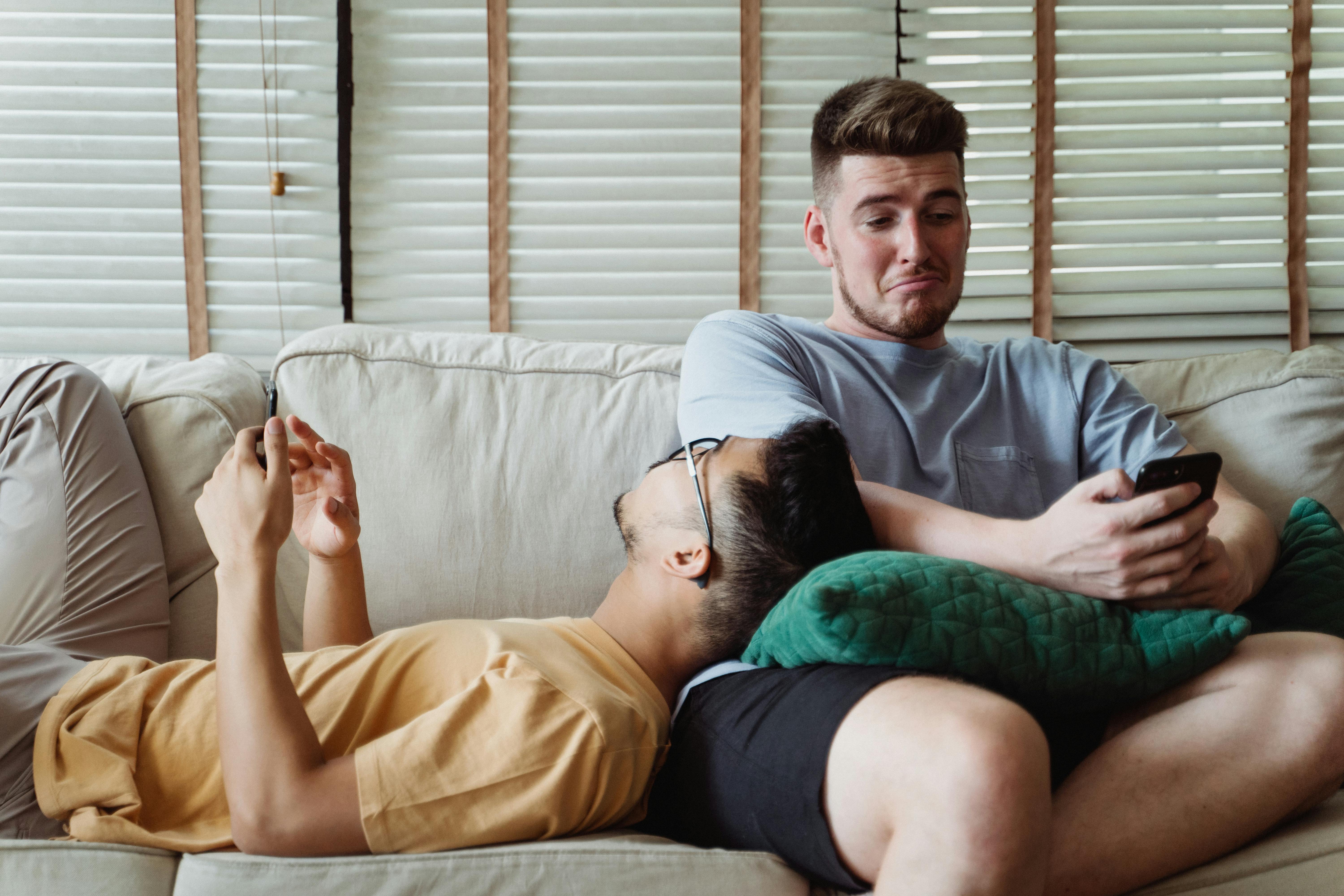 two men using smartphones and relaxing on a couch