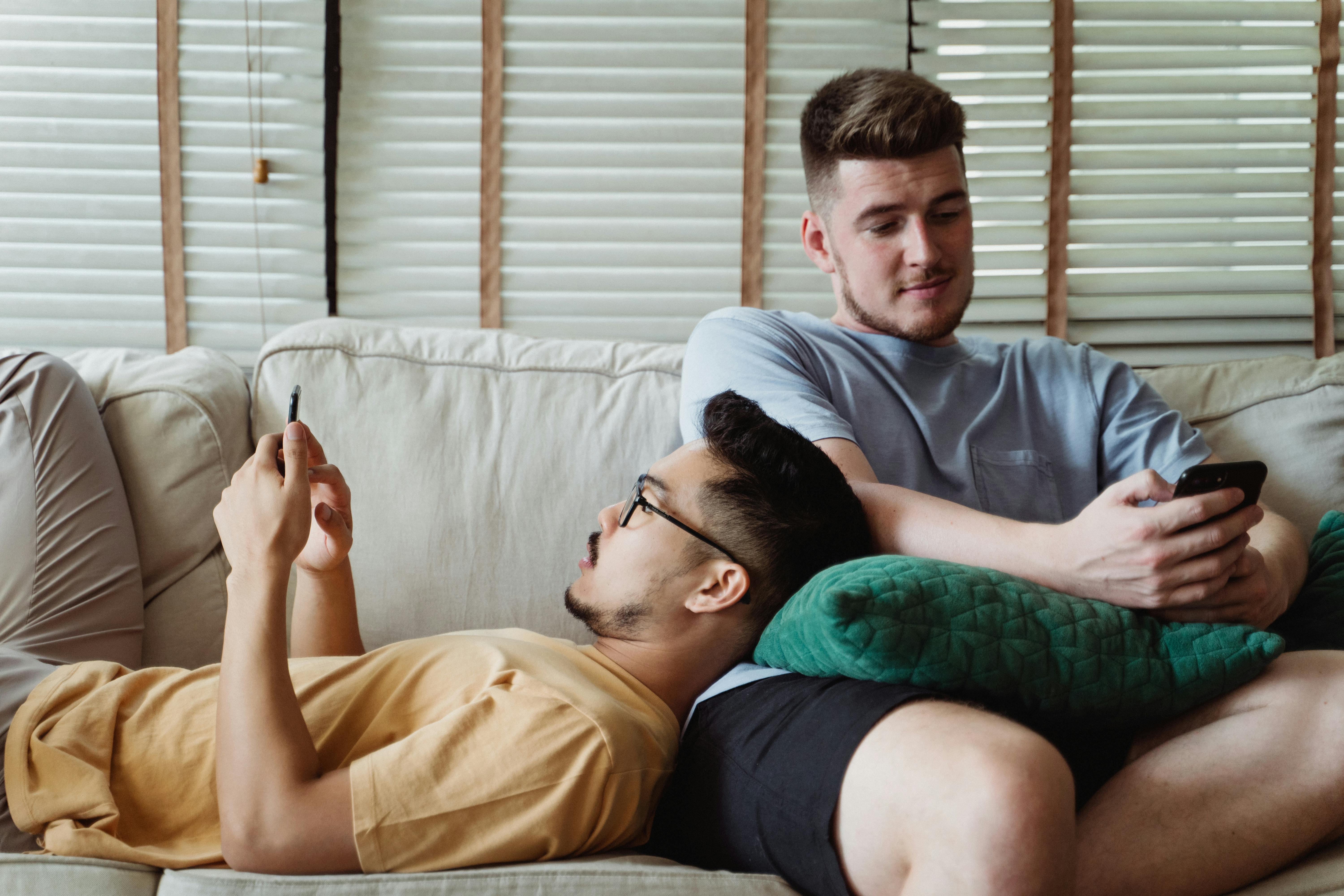 two men using smartphones and relaxing on a couch