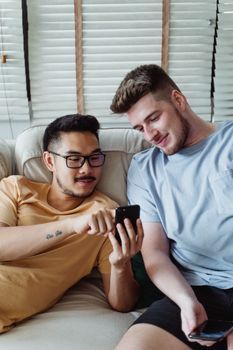 一对快乐、多元化的夫妇在室内的沙发上放松，一边笑着一边看手机内容