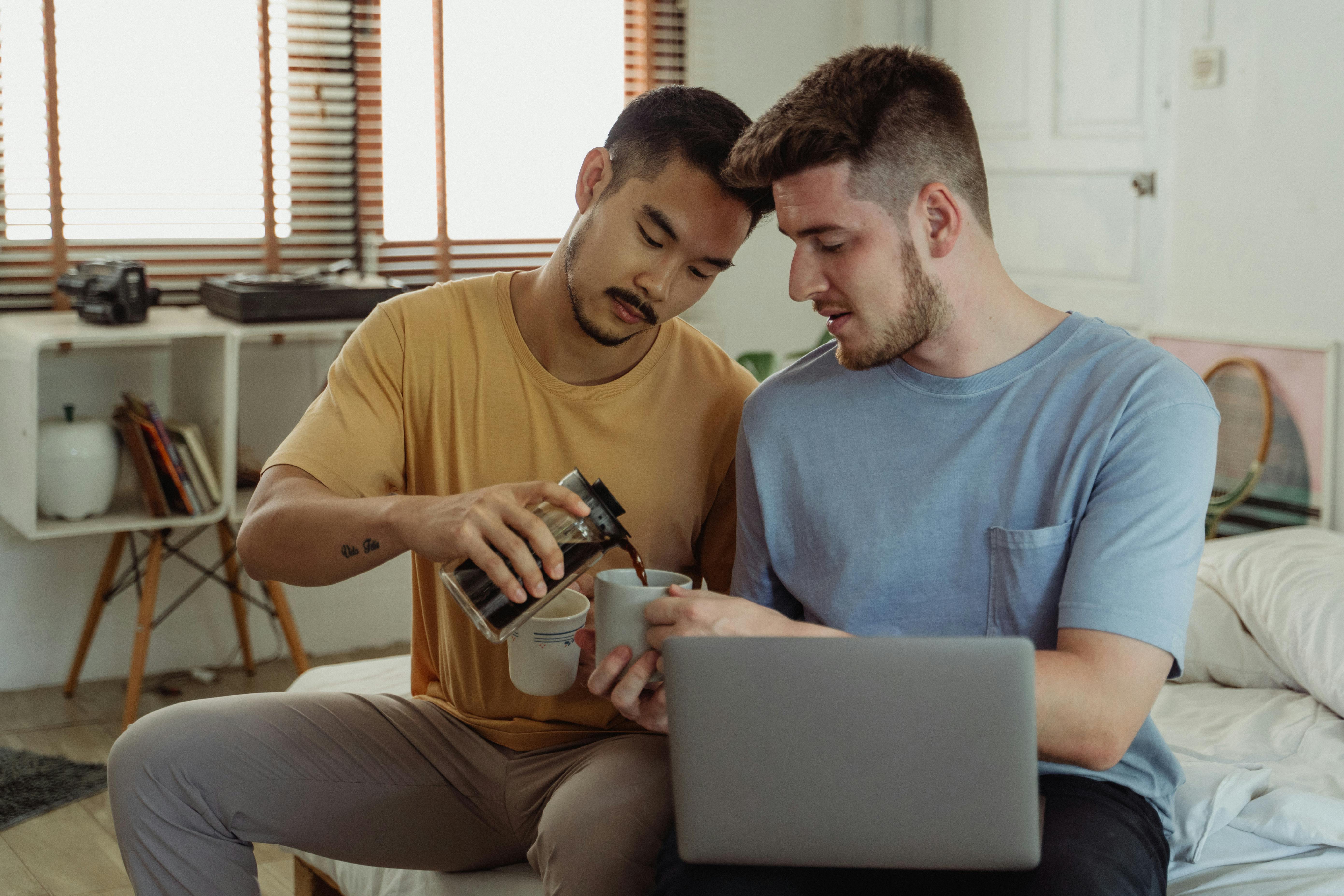 卧室里，两名男子正在放松身心，一个在倒咖啡，另一个在用笔记本电脑