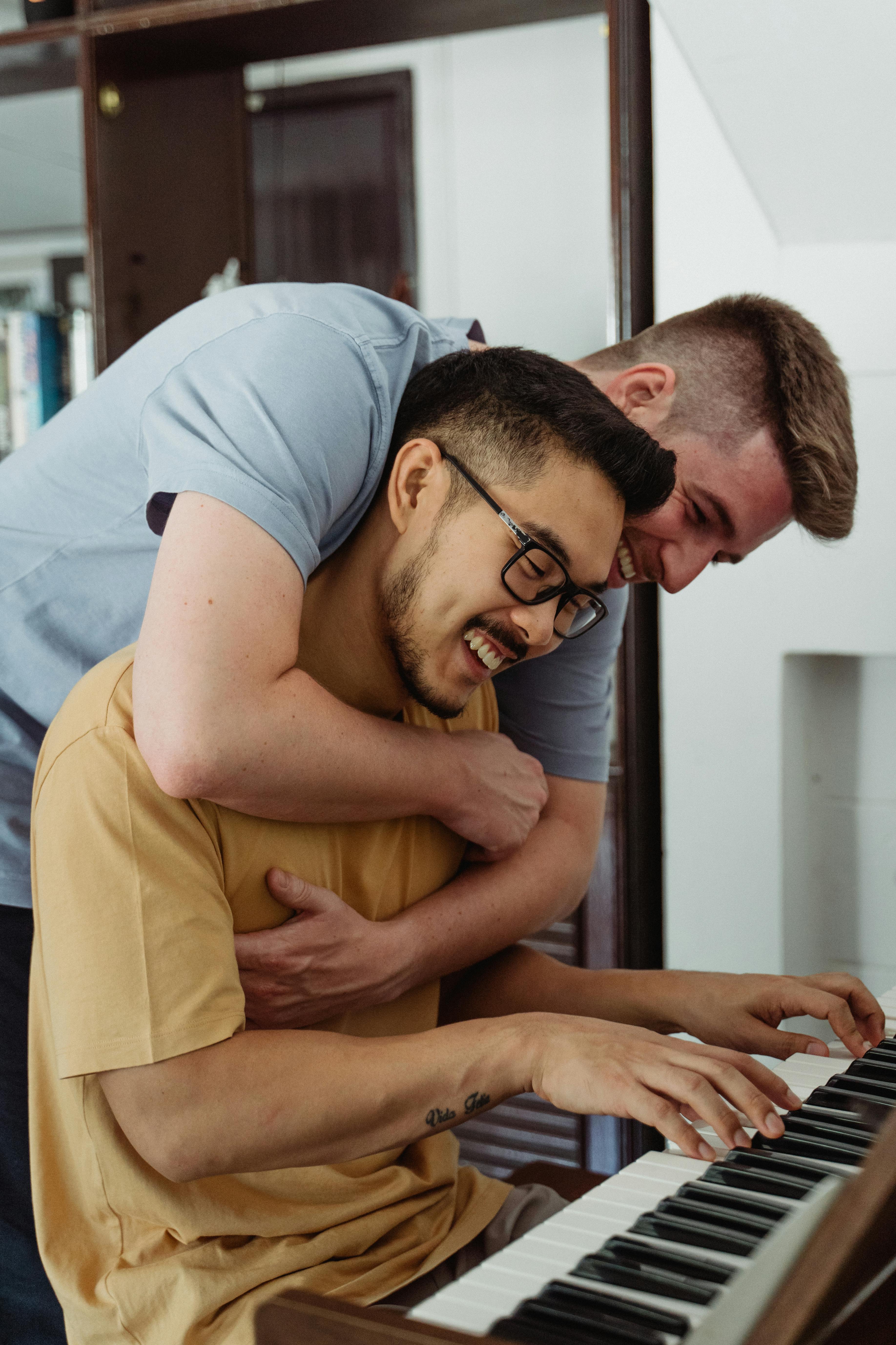 man hugging another man playing the piano