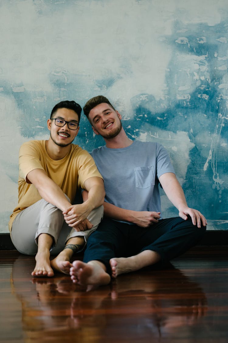 A Couple Of Men Sitting On A Wooden Floor Leaning On The Wall