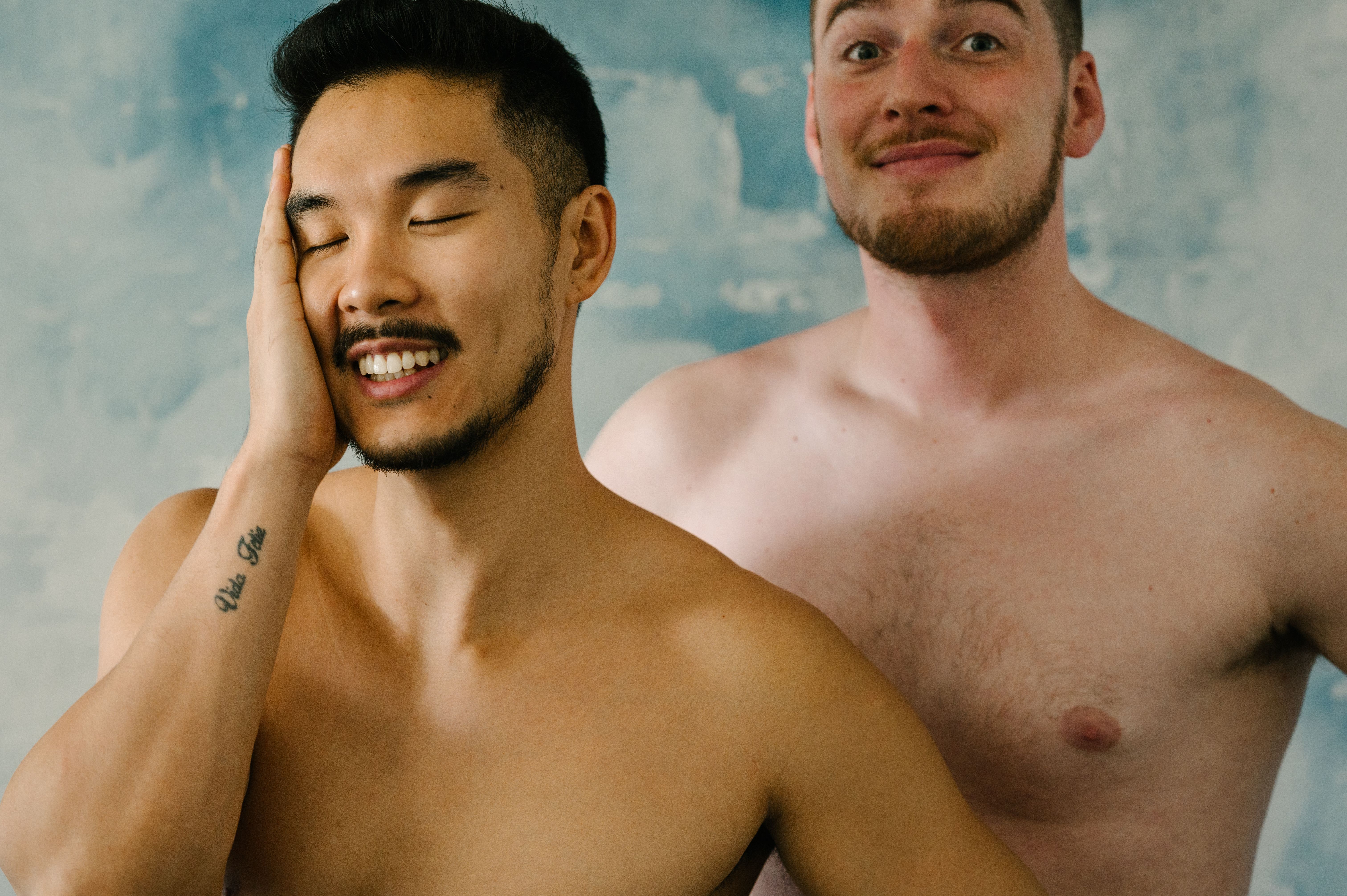 A joyful interracial couple engaged in a playful, shirtless portrait showing affection and happiness.