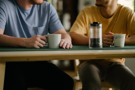 Two friends enjoy coffee together at a wooden table indoors, fostering connection.