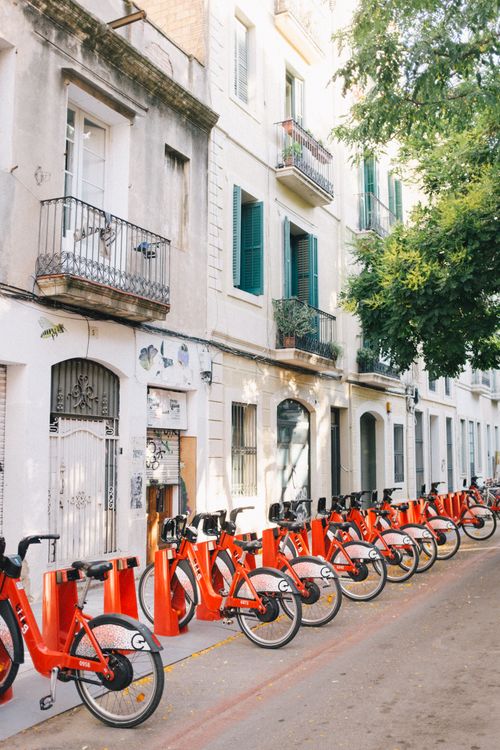 Free Rows of red bicycles on a charming Barcelona street with balconies and greenery. Stock Photo