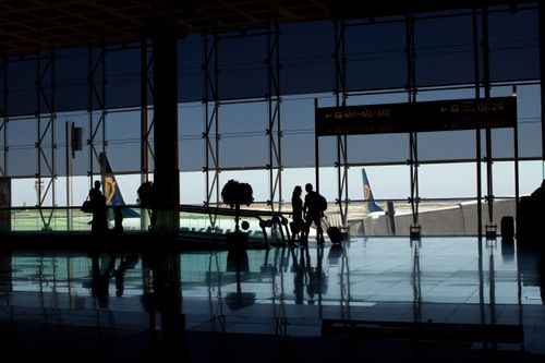 Free Travelers silhouetted in a modern airport terminal with glass windows and visible airplane tails. Stock Photo