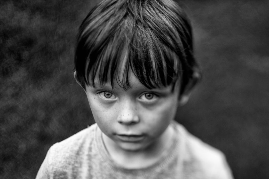 Close-up black and white portrait of a young boy with captivating eyes and messy hair.