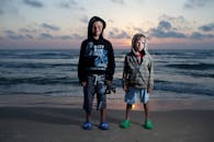 日落时分，两个孩子穿着连帽衫和泡沫木鞋站在以色列的海滩上