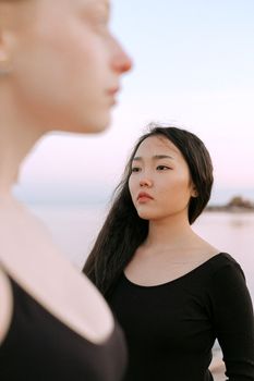 日落时分，两名女子静静伫立在宁静的海滩旁，眼前是自然美景，心中一片安宁
