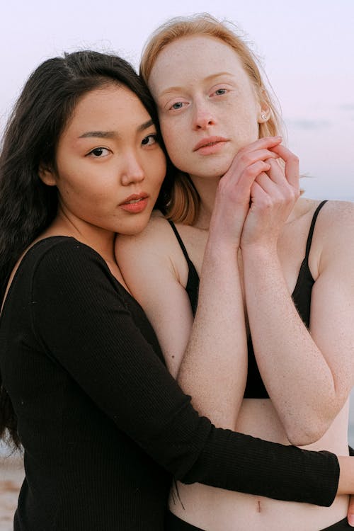 A Woman in Black Long Sleeve Shirt Hugging a Woman in Black Bikini