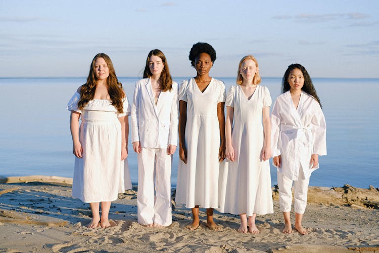 Group Of Women Wearing White Clothes Standing On A Sand