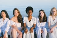一群身着白色服装的多元化女性坐在海边，展现着团结与平静