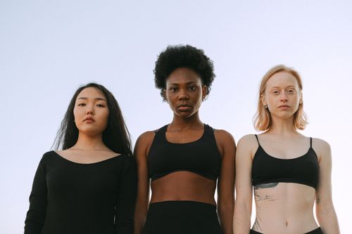 Free Three diverse women confidently standing under a clear sky, embracing unity and strength. Stock Photo
