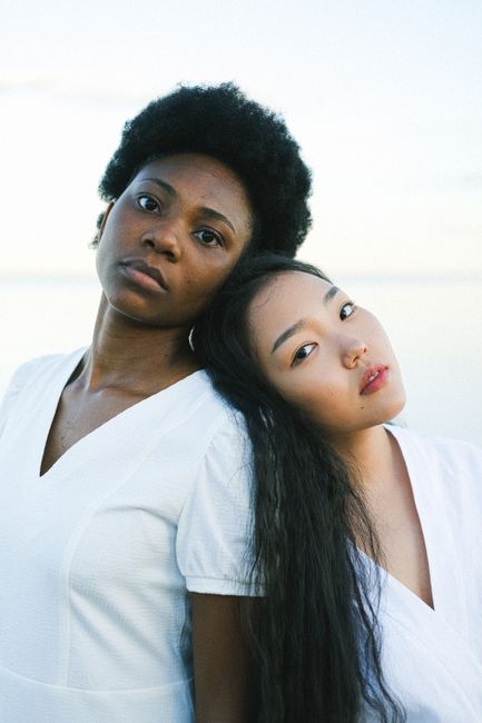 Two women embrace friendship by the waterfront, symbolizing diversity and unity.