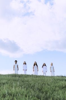 五名身着白衣的妇女站在蓝天下的绿色山坡上